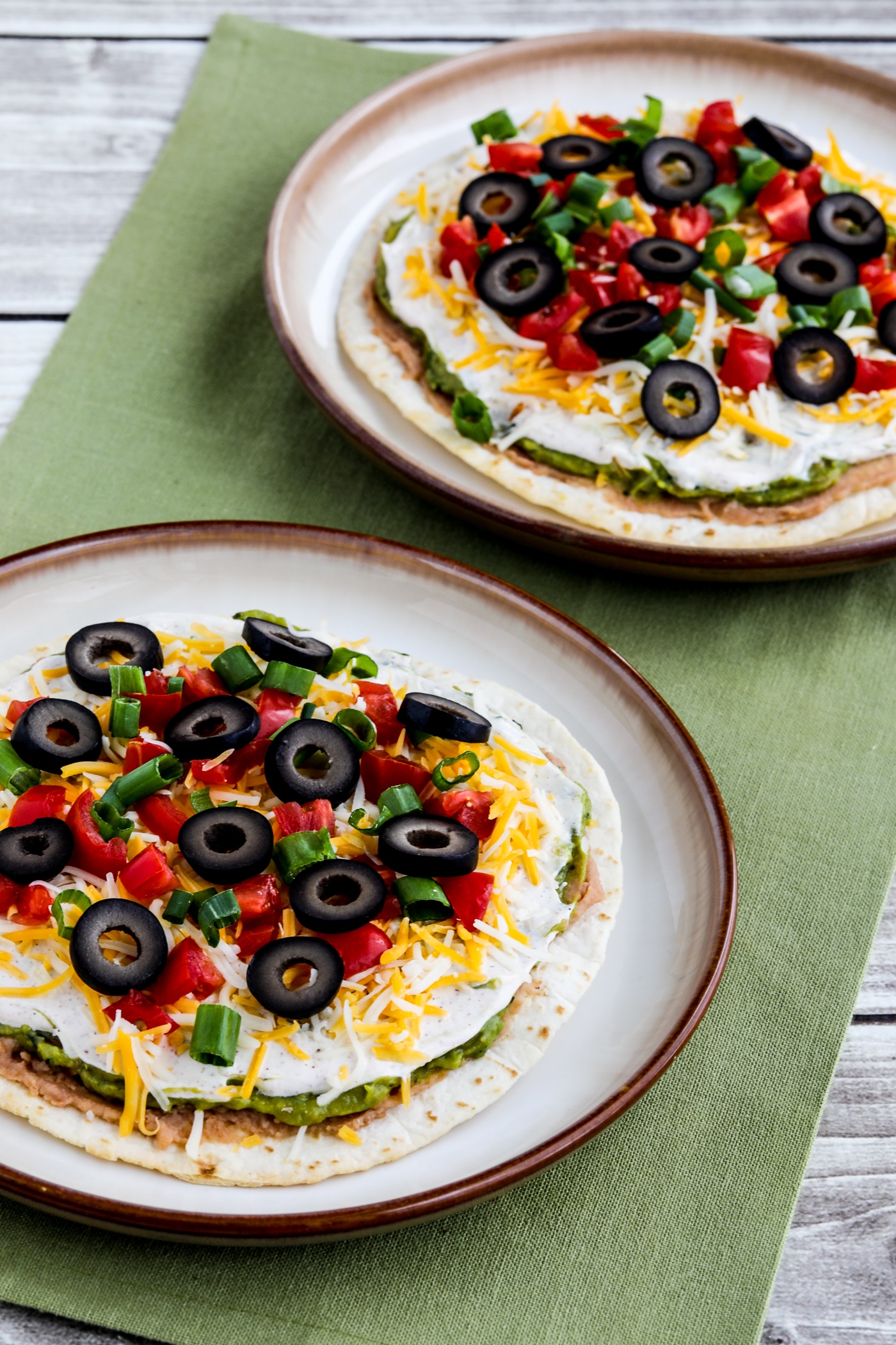 Seven Layer Dip Tostadas shown on two serving plates with green napkin