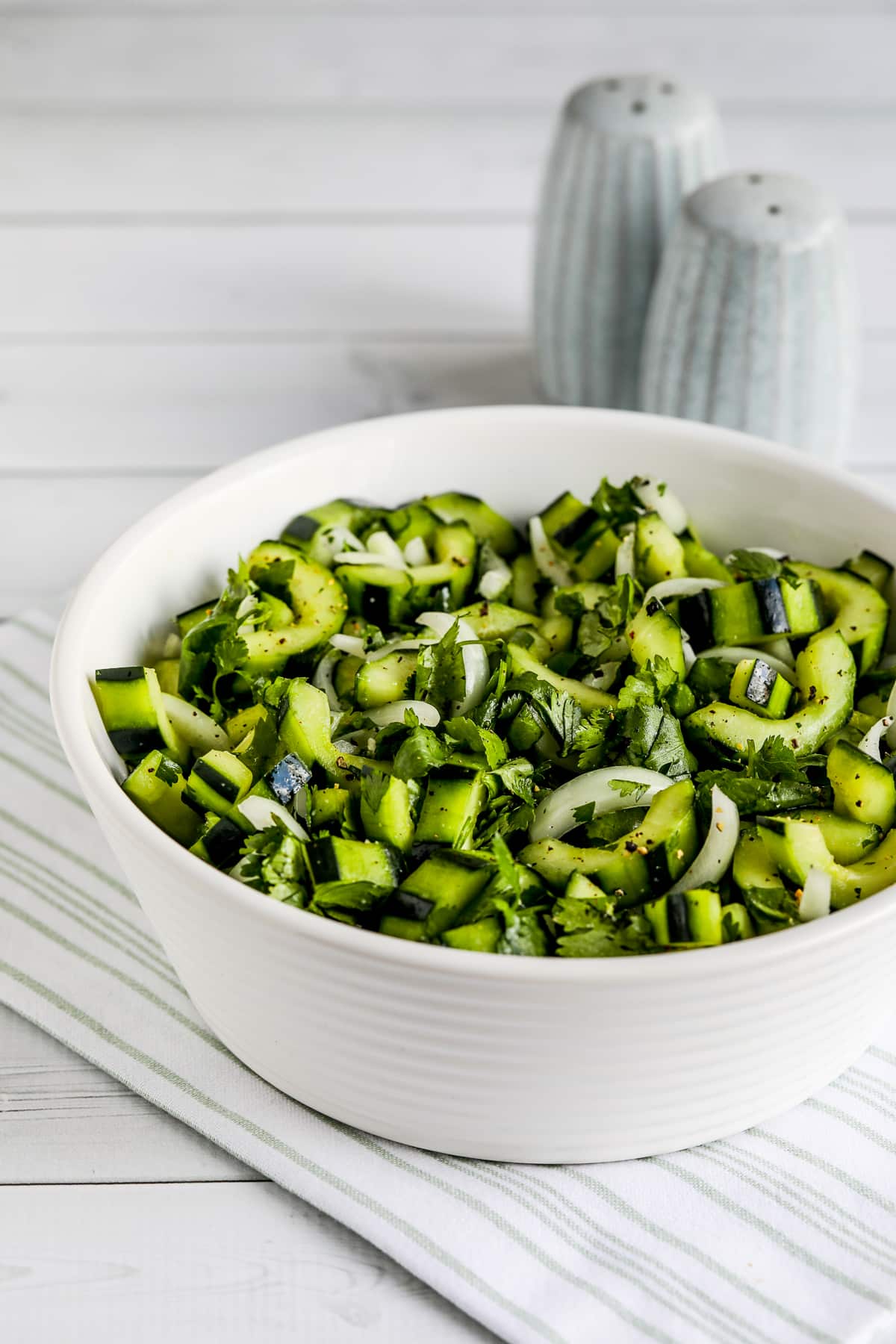 Asian Cucumber Salad in serving bowl with salt-pepper in background.