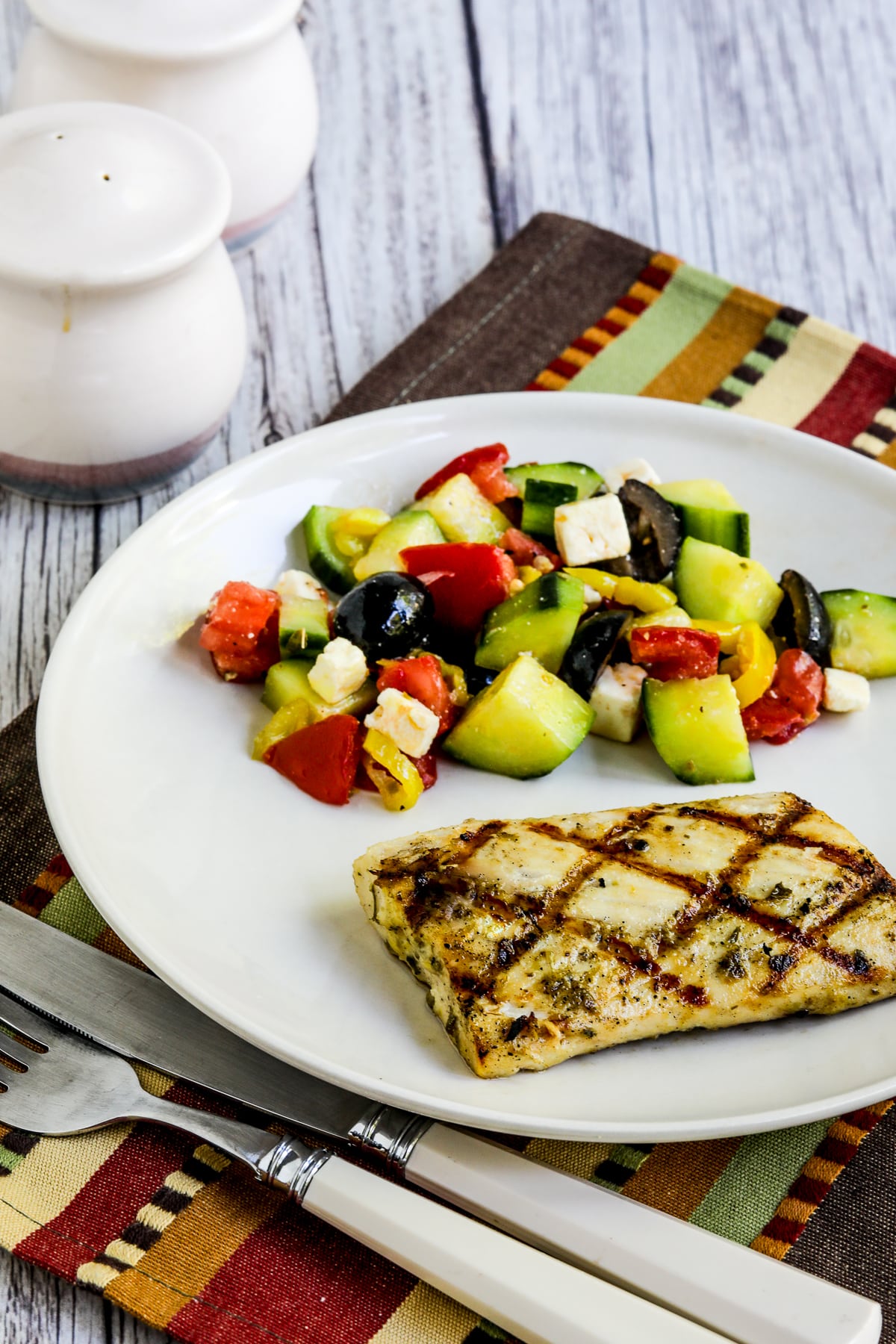 Grilled fish, lemon and capers are shown on a plate with salad.