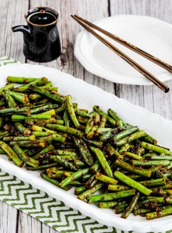 Spicy Szechuan Green Beans shown on serving plate with chopsticks and soy sauce in background
