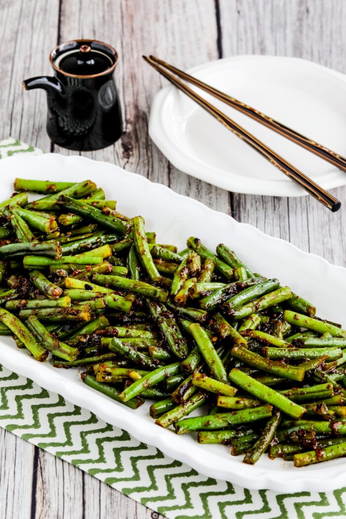 Spicy Szechuan Green Beans shown on serving plate with chopsticks and soy sauce in background