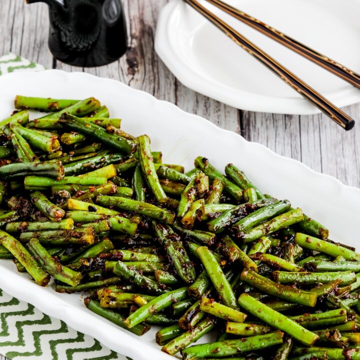 Spicy Szechuan Green Beans shown on serving plate with chopsticks and soy sauce in background