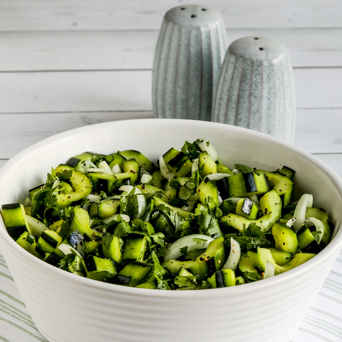 Asian Cucumber Salad shown in serving bowl with salt-pepper in back.