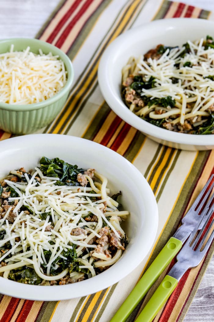 close-up photo of Pasta with Sausage and Kale with Palmini Pasta, in two serving bowls with parmesan