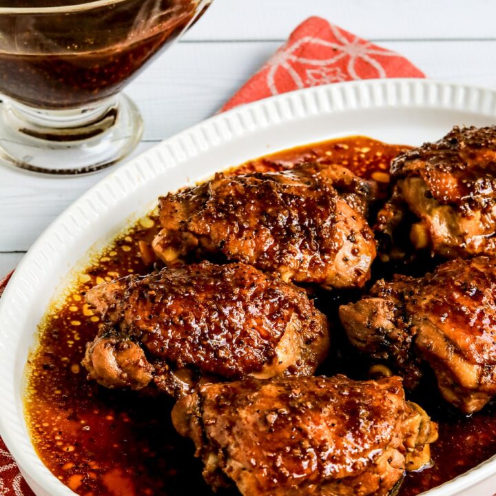 Filipino Chicken Adobo covered in sauce, shown on serving plate with sauce in back.