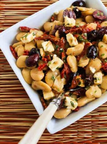 Square image for Butter Bean Salad shown in serving bowl with fork on colorful mat.