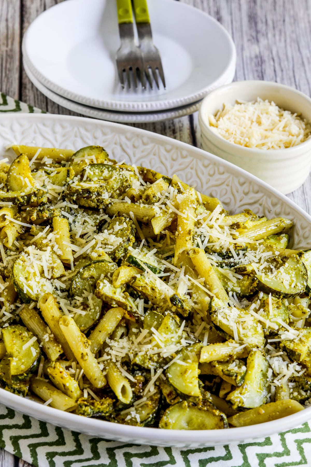 Penne pasta with zucchini and pesto on a serving plate with parmesan cheese