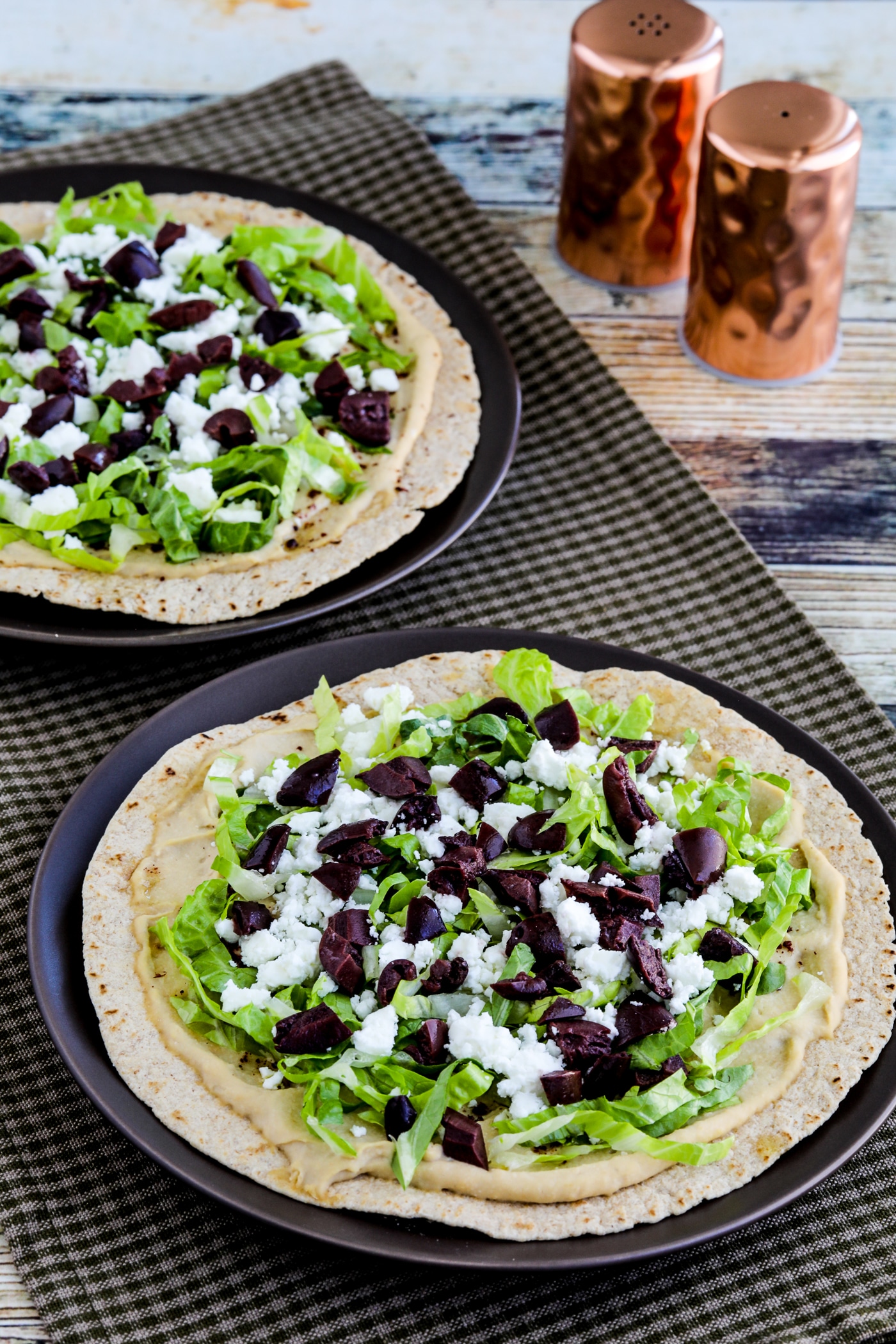 Middle Eastern Tostadas with Hummus and Feta shown on two serving plates with salt-pepper in background