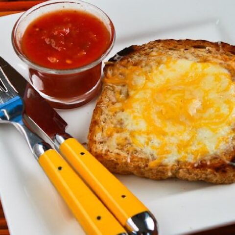 Cheesy Eggs in a Hole shown on plate with salsa, knife, and fork