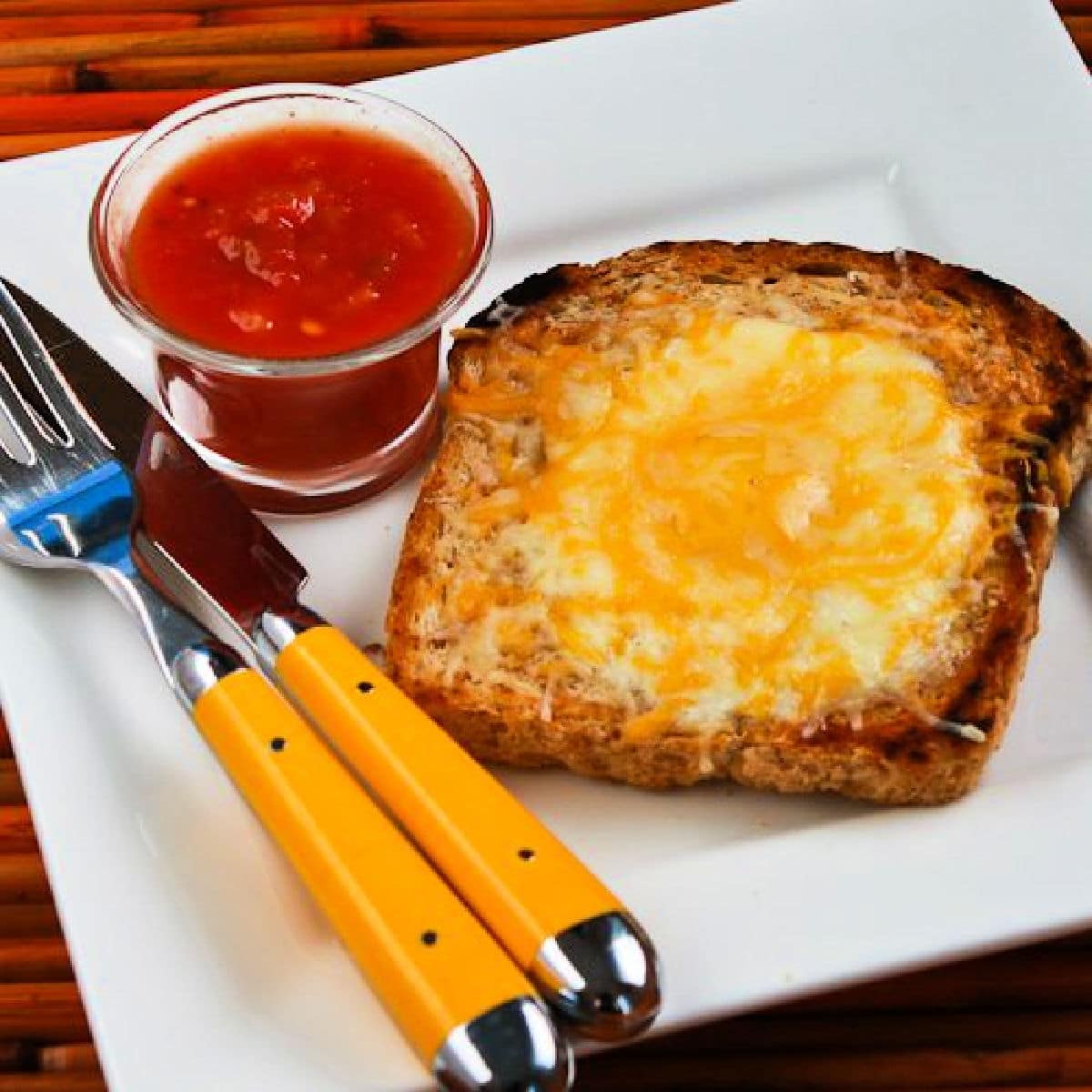 Square image of Cheesy Eggs in a Hole on serving plate with salsa.
