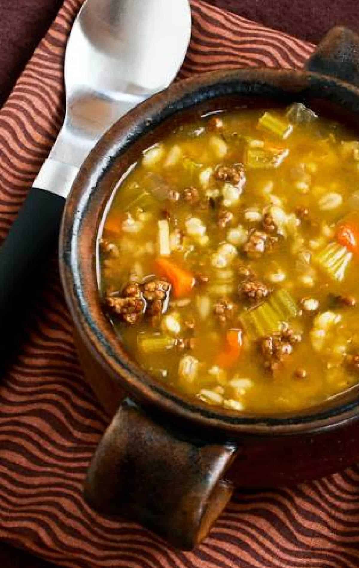 Ground Beef Barley Soup shown in brown soup bowl