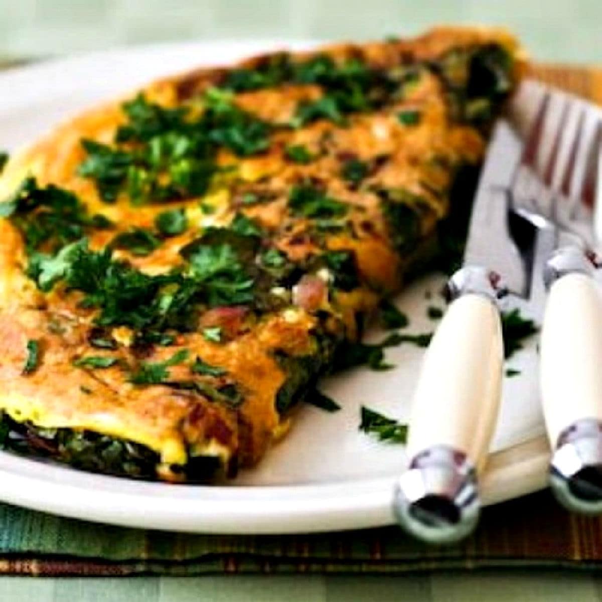 Kale Omelet with Cheese shown on serving plate with knife and fork.