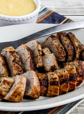 Pan-fried pork tenderloin with creamy mustard sauce shown on serving platter with fork and sauce in back.