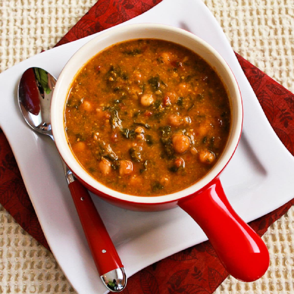 Square image for Tomato Chickpea Soup shown in bowl on plate with spoon.