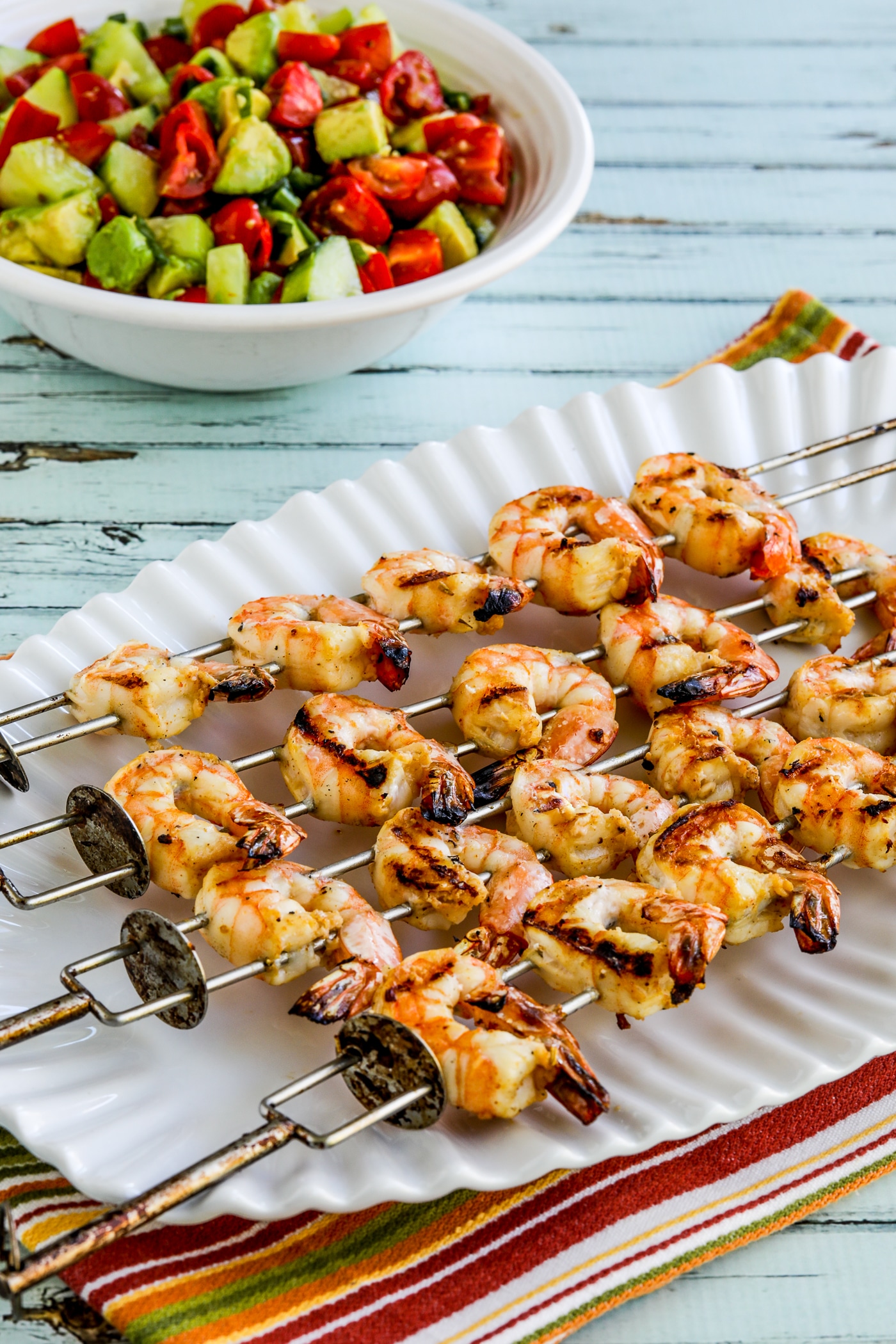 Grilled shrimp skewers on a serving plate with sauce in a bowl