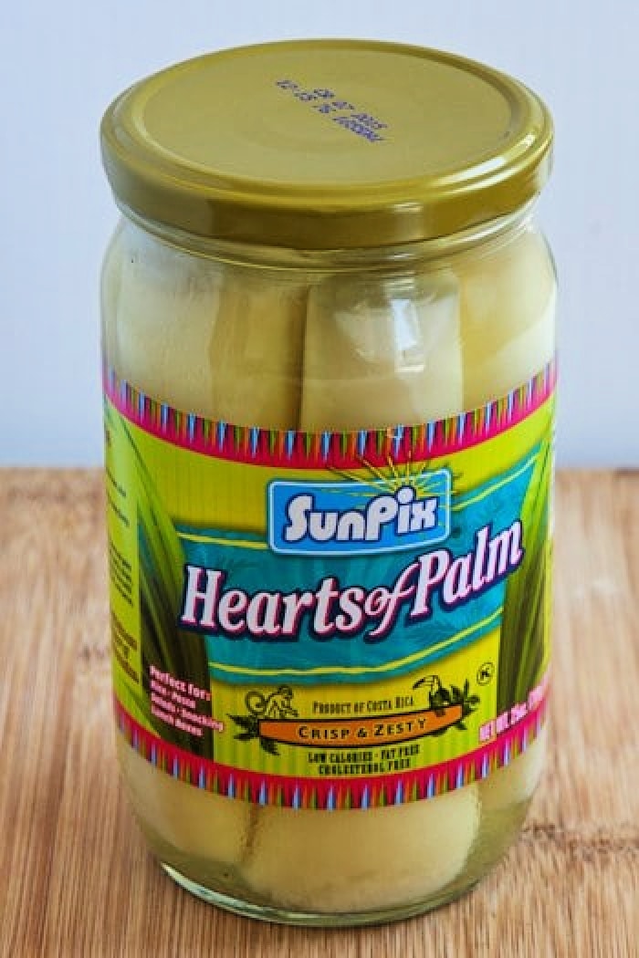 A large jar of palm hearts on a cutting board.