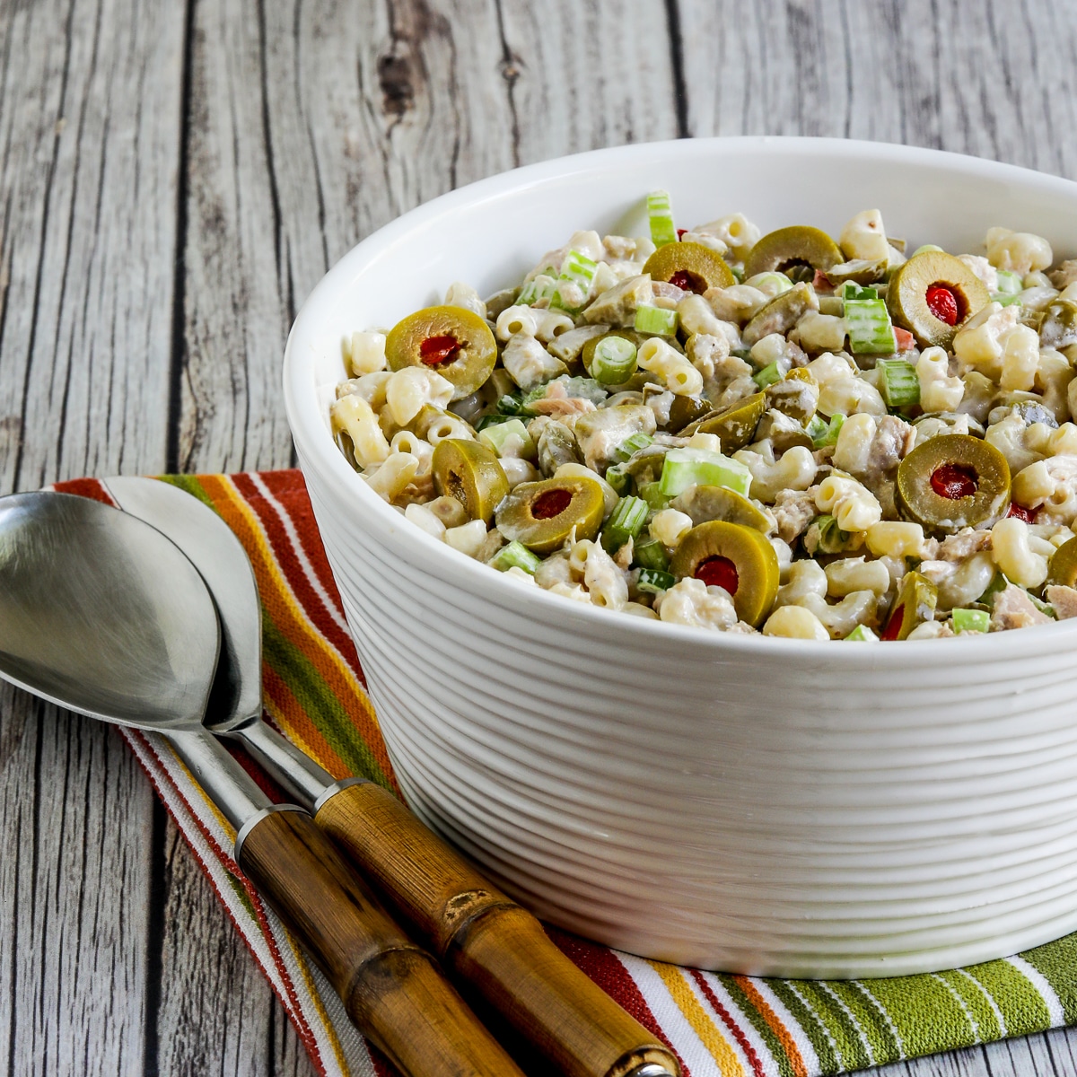 Square image of tuna pasta salad with green olives in a serving bowl.