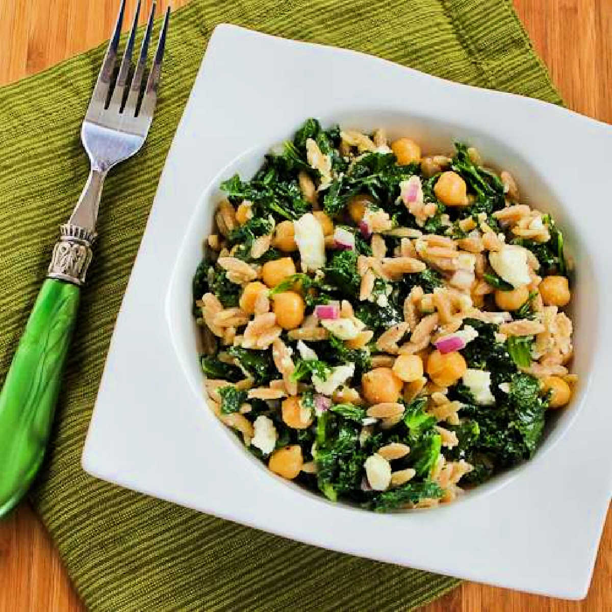 Square image of Orzo Salad with Chickpeas and Kale shown in white serving bowl on green napkin.