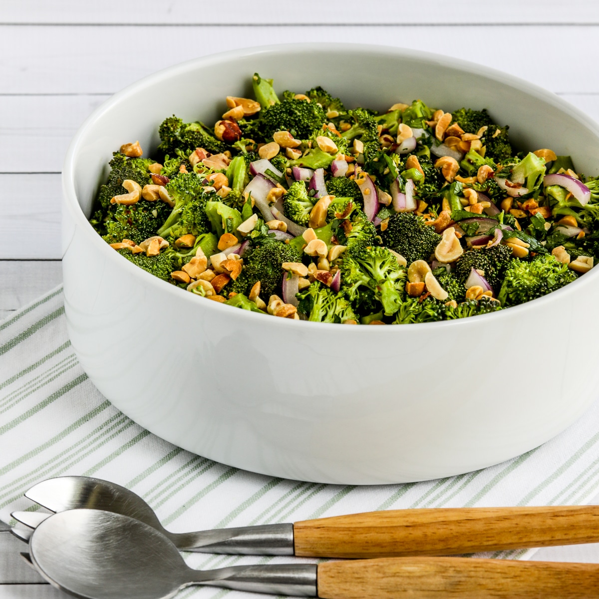 Square image of Broccoli Salad in serving bowl on napkin with fork and spoon for serving.