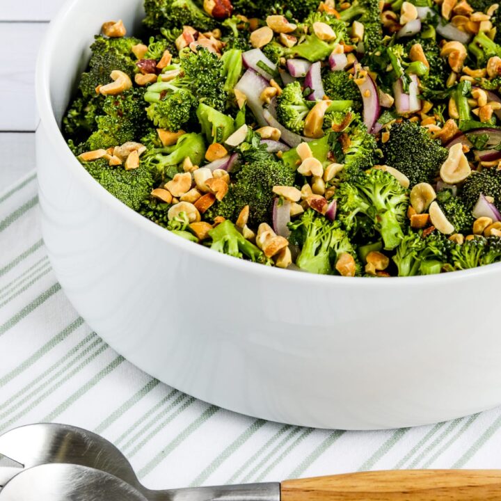Asian Broccoli Salad in serving bowl on napkin with serving fork and spoon.