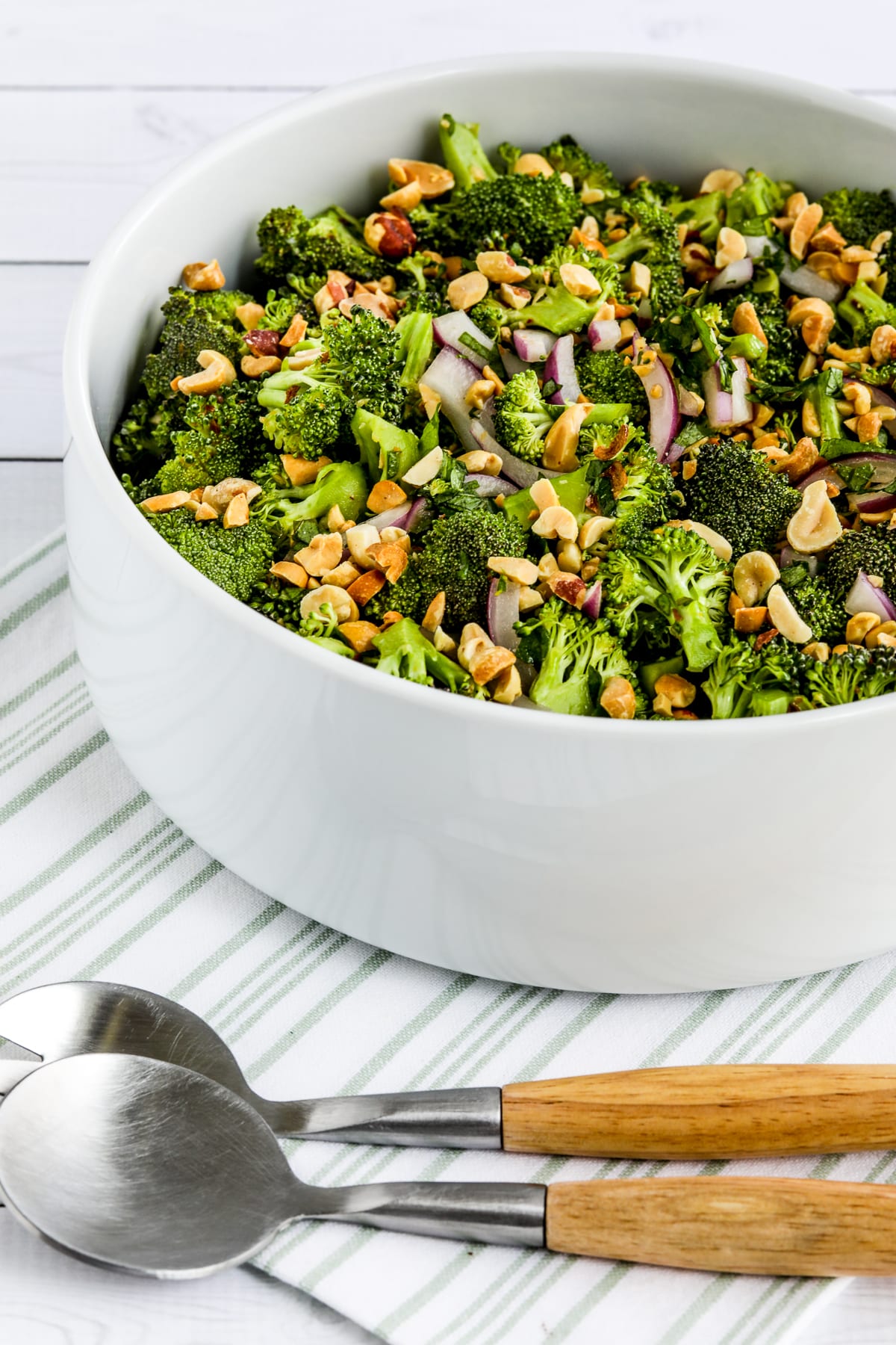Broccoli Salad in serving bowl on napkin with serving fork and spoon.