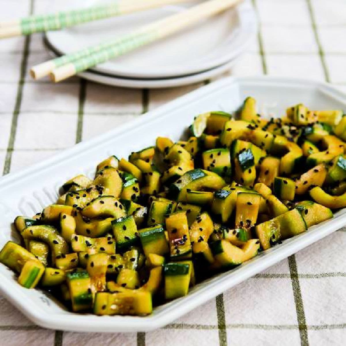 Chinese Cucumber Salad shown on rectangular serving platter, with plates and chopsticks in back.