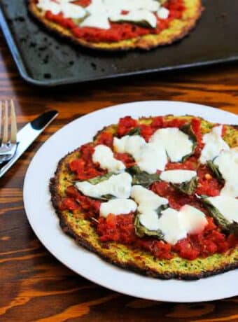 Square image of Zucchini Crust Pizza Margherita shown on serving plate with baking sheet in back.
