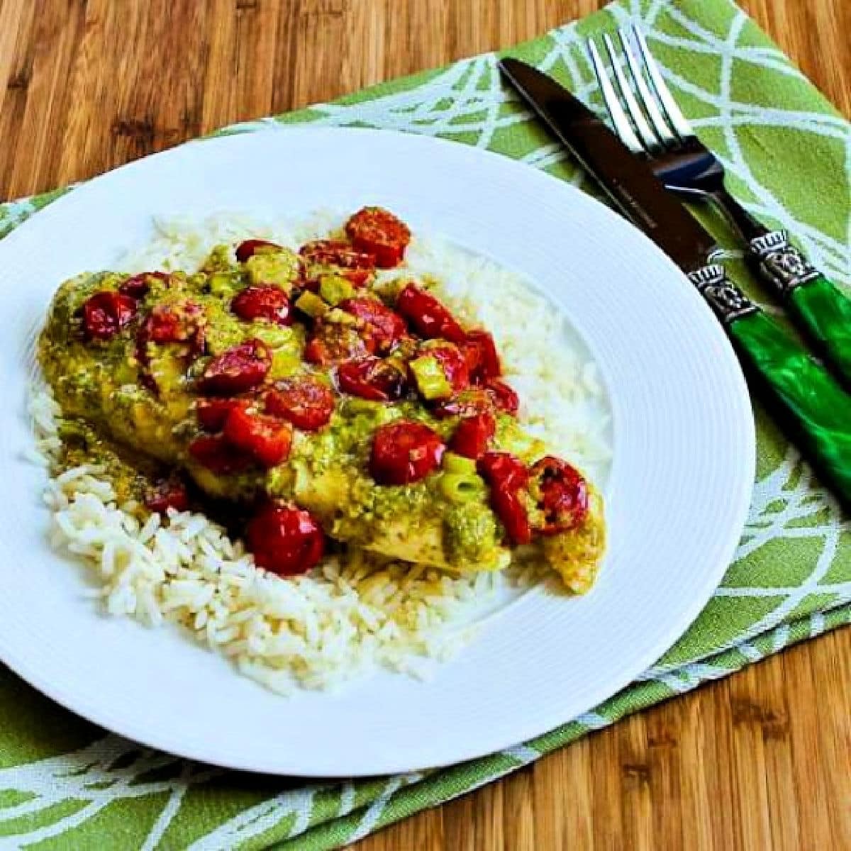 Square image of Baked Fish in Foil with Pesto and Tomatoes on serving plate over rice.