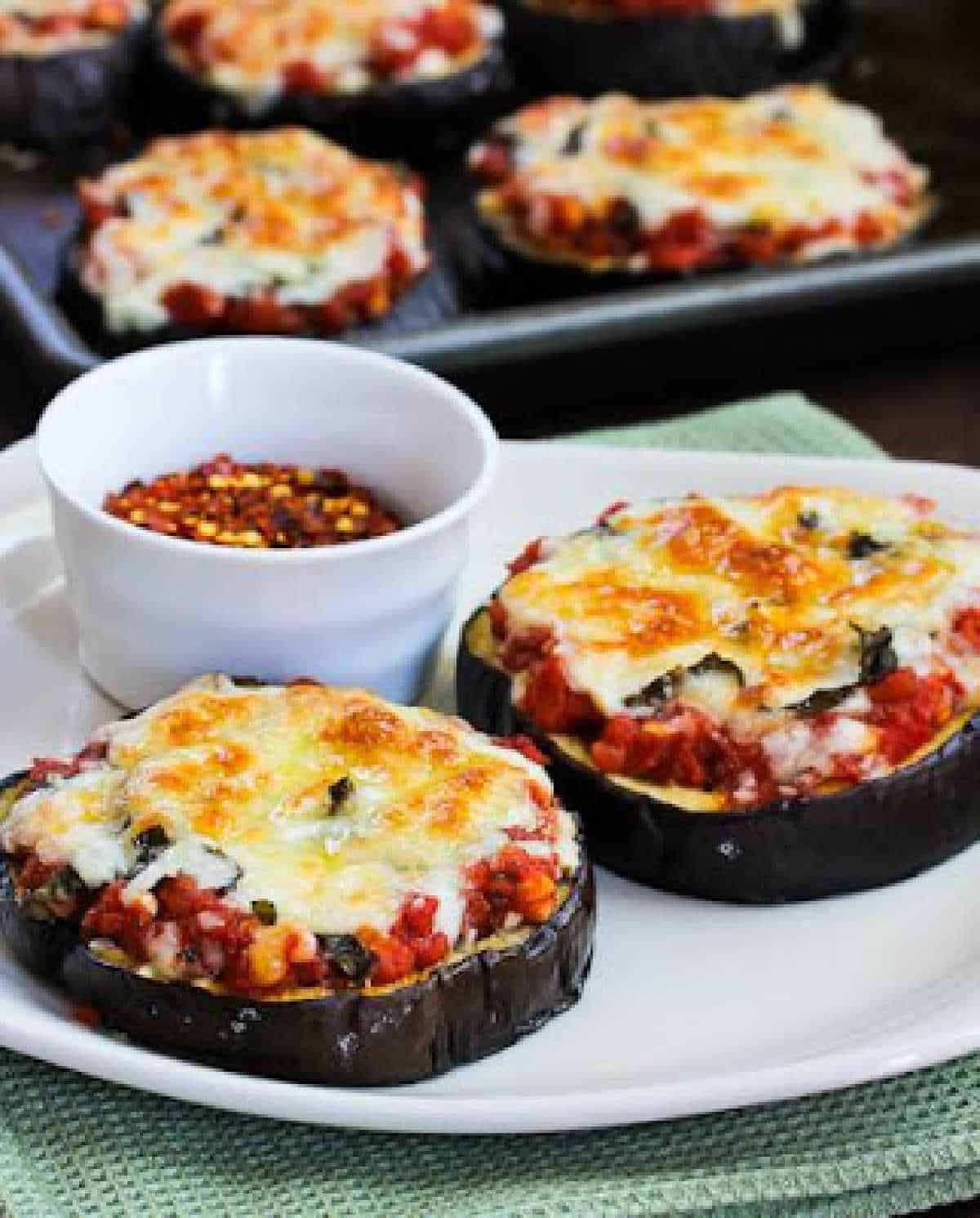 eggplant pizza on serving plate with baking dish with more pizzas in background