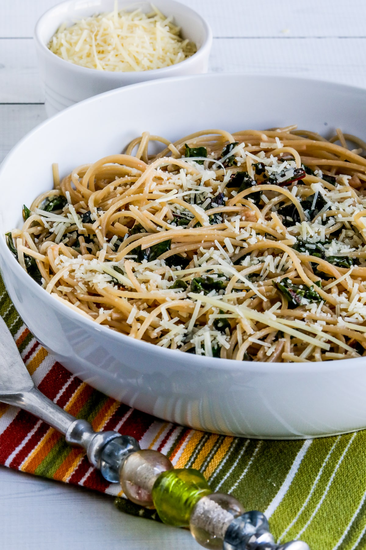 Spaghetti with Garlic, Chard, and Cheese, shown in serving bowl with spoon and Parmesan cheese.