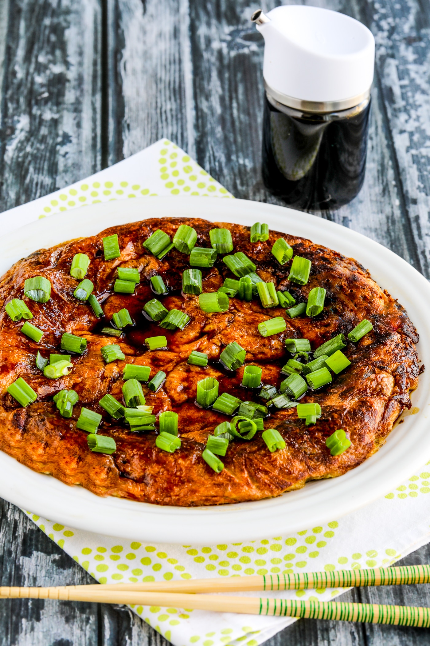 Chicken Egg Foo Yung on serving plate with soy sauce dispenser and chopsticks