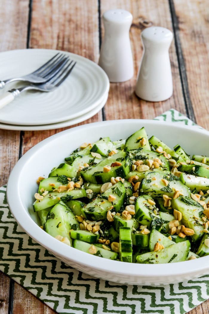 Thai Cucumber Salad in serving bowl with plates, forks, salt, and pepper