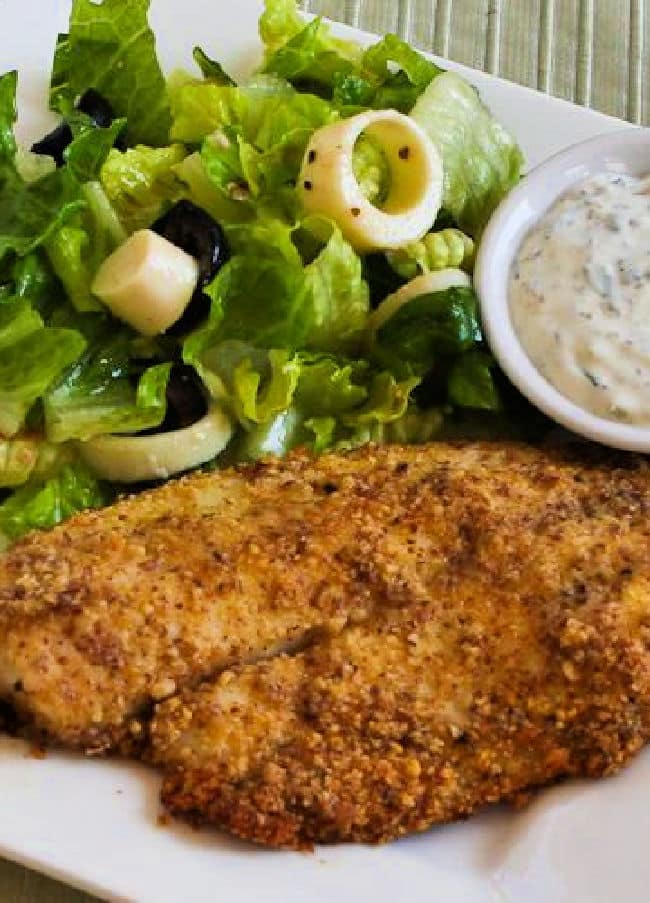 Cropped image of Almond and Parmesan Baked Fish on serving plate with tartar sauce and salad.