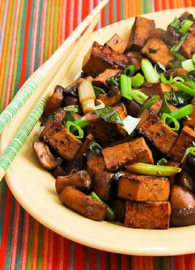 Stir-Fried Marinated Tofu and Mushrooms on serving plate with chopsticks and striped background.