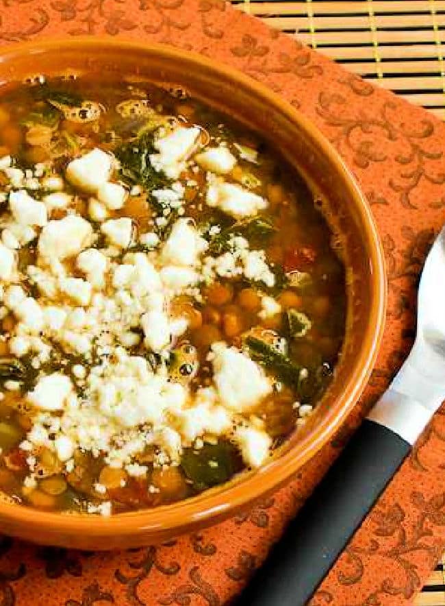 Slow Cooker Greek Lentil Soup in bowl with spoon, cropped image.
