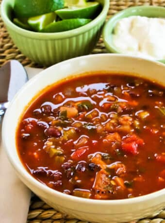 Square image for Chicken Black Bean Soup shown in bowl with lime and sour cream in back.