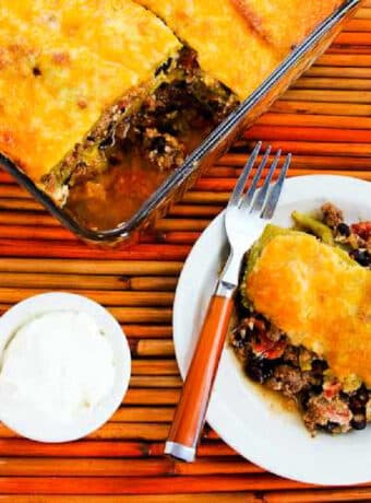 Mexican Ground Beef Casserole with Beans, and Chiles shown on serving plate with casserole dish in back.