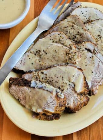 Square image of Slow Cooker Bavarian Pork Roast shown on serving plate with fork and gravy in background.