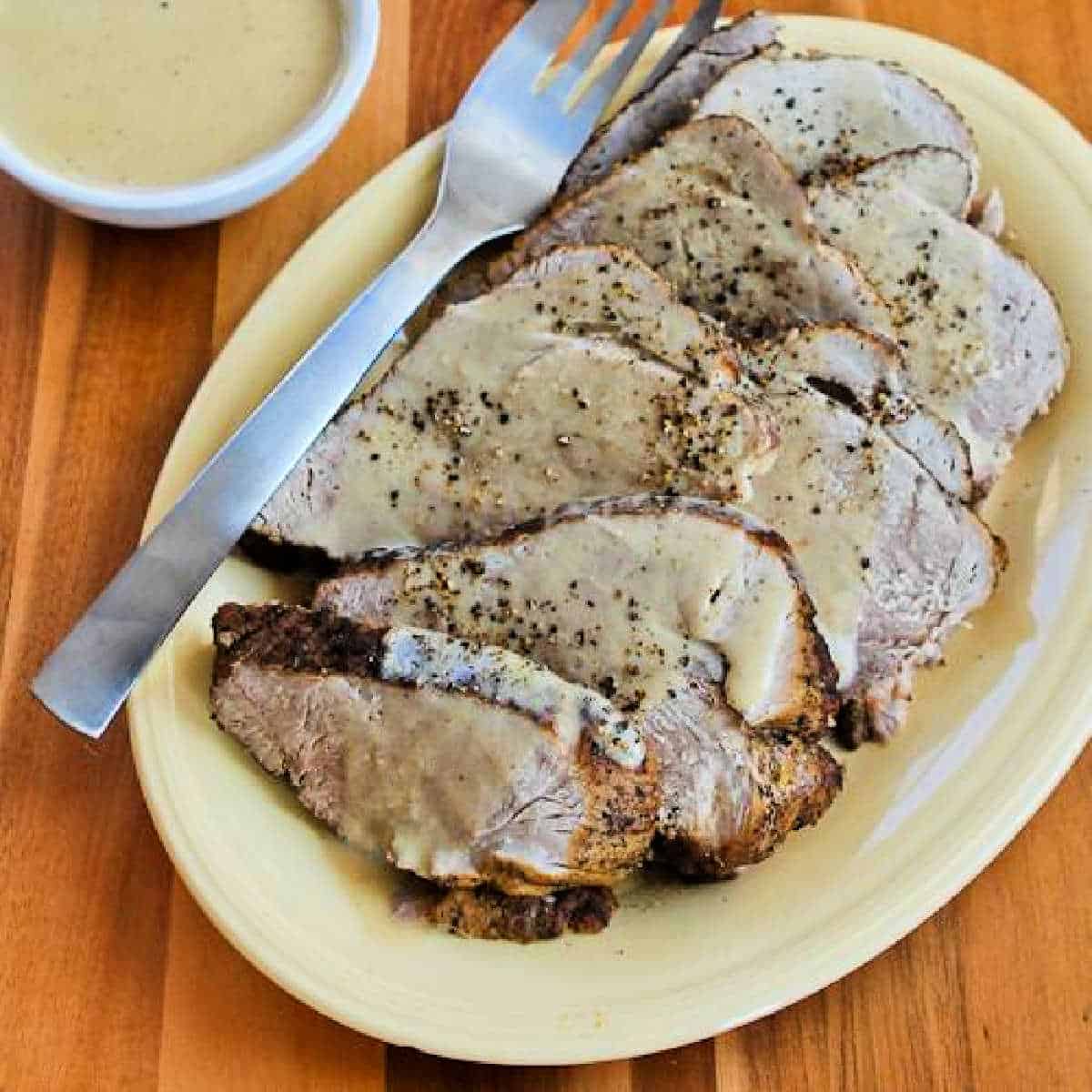 Square image of Slow Cooker Bavarian Pork Roast shown on serving plate with fork and gravy in background.