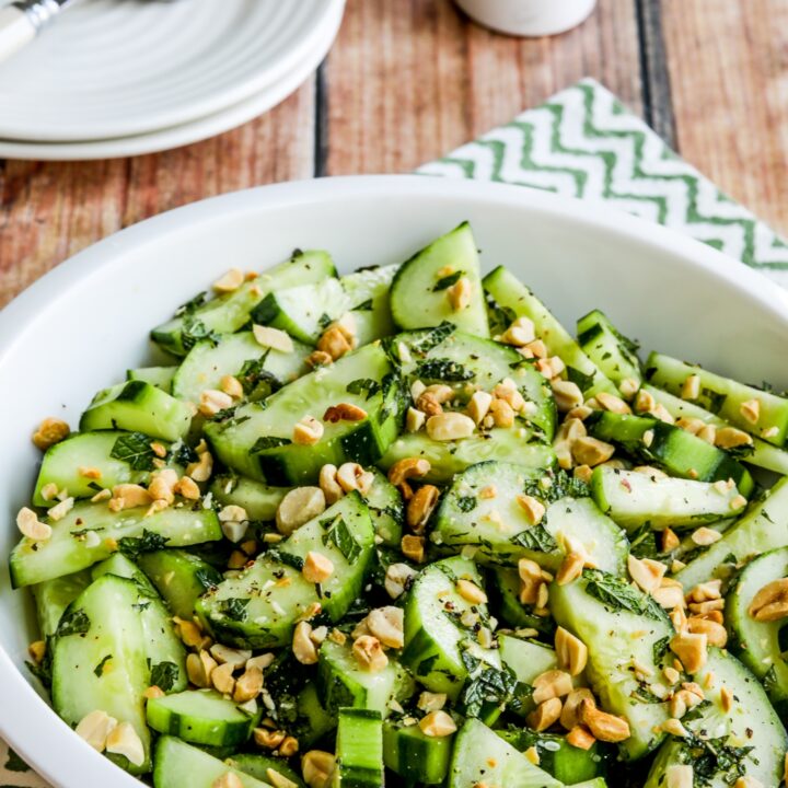 Thai Cucumber Salad close-up photo in serving bowl with plates, forks, salt, and pepper.