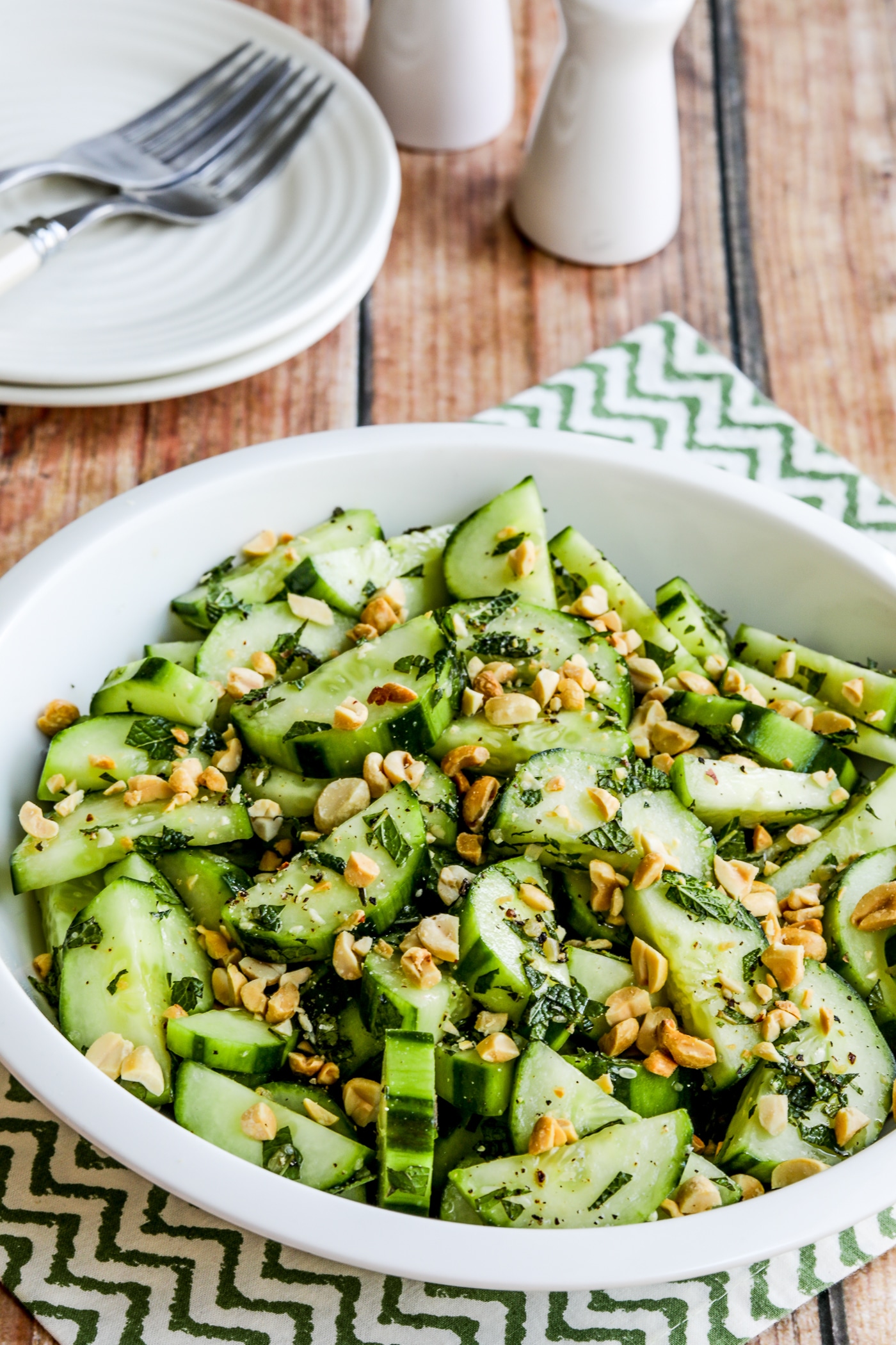 Thai Cucumber Salad close-up photo in serving bowl with plates, forks, salt, and pepper.