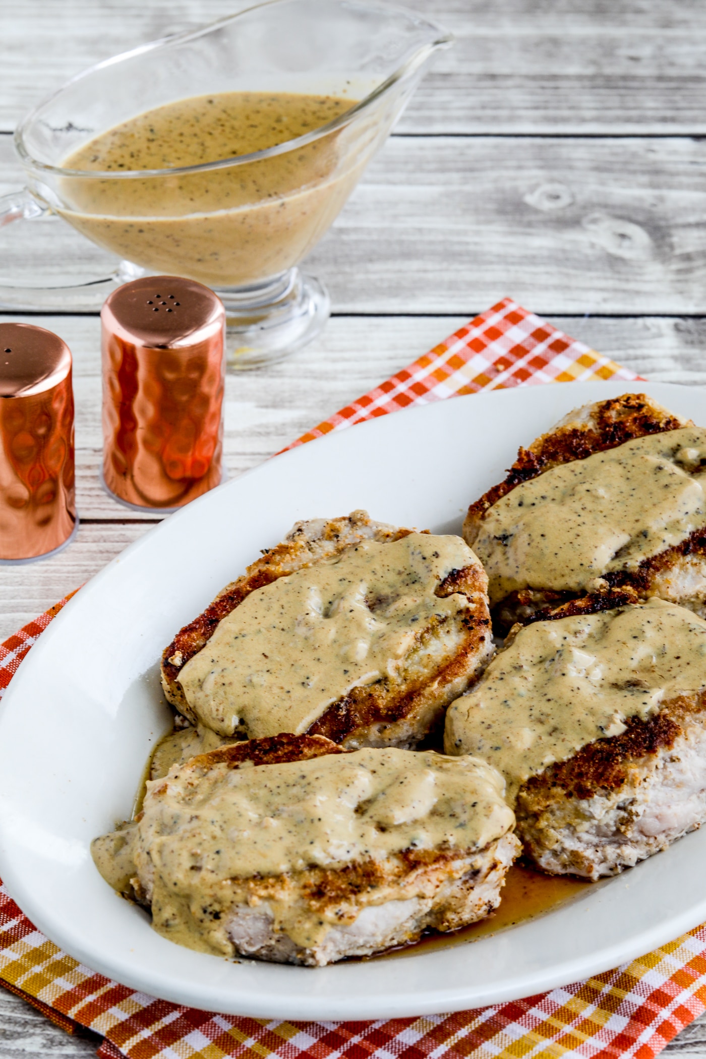 Grain-free breaded pork chops laid out on a serving platter with gravy, gravy, and salt and pepper shakers