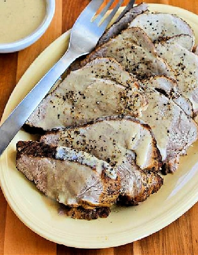 Slow Cooker Bavarian Pork Roast shown on serving plate with fork and sour cream gravy on the side