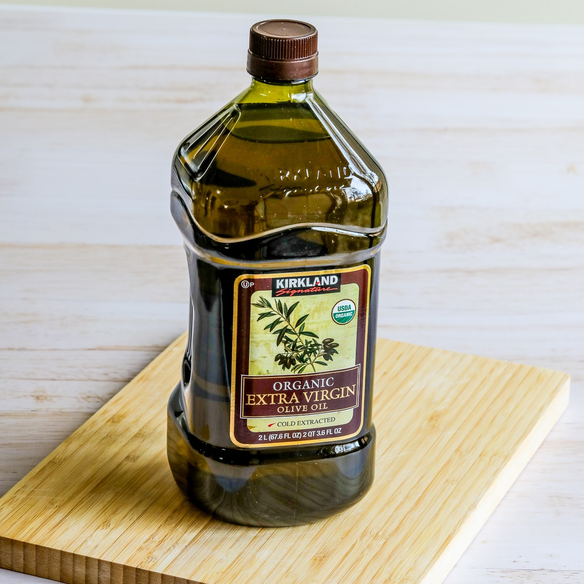 Kirkland Organic Extra-Virgin Olive Oil square image of olive oil bottle on cutting board.