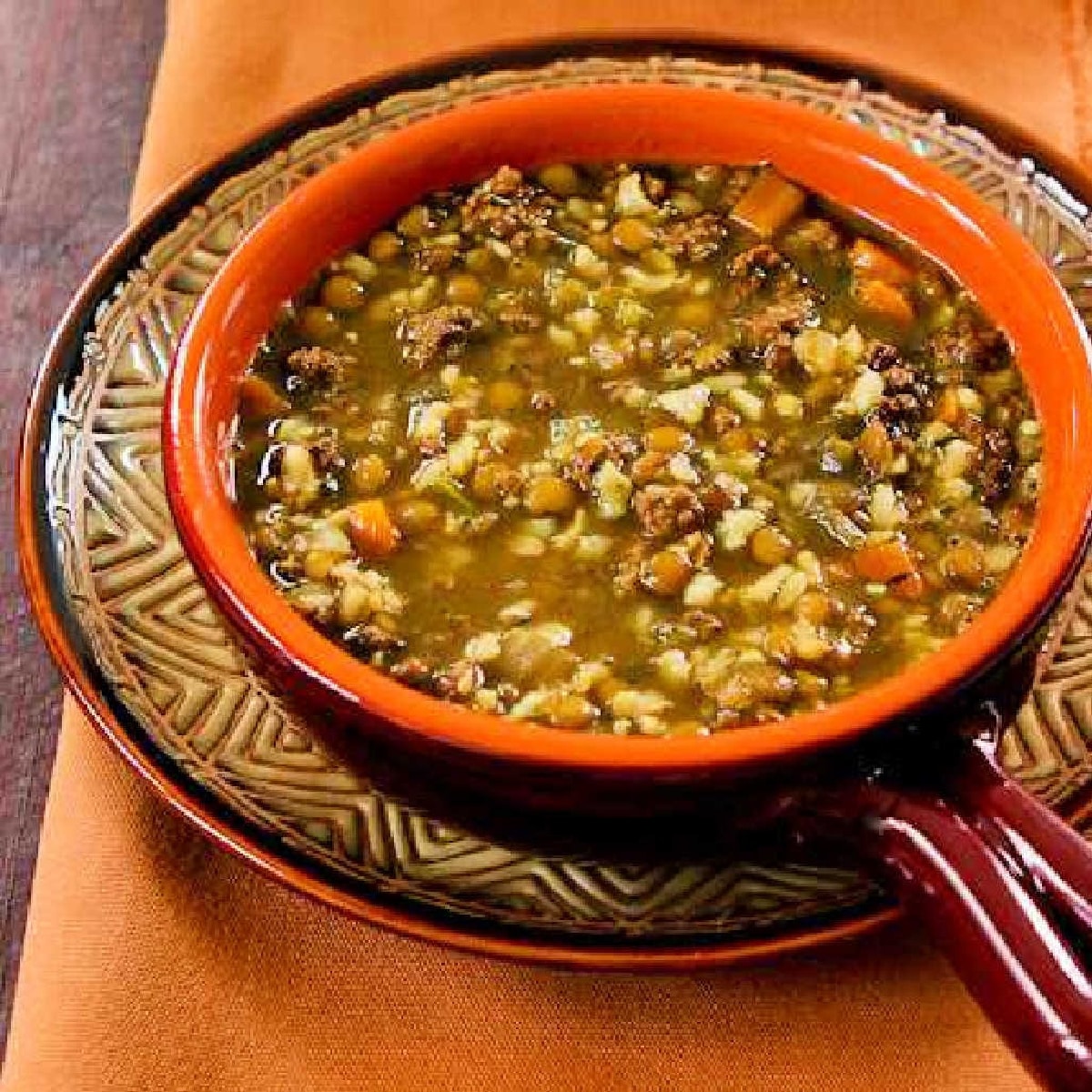 Square image of Lentil Soup with Ground Beef shown in soup bowl on decorative plate.