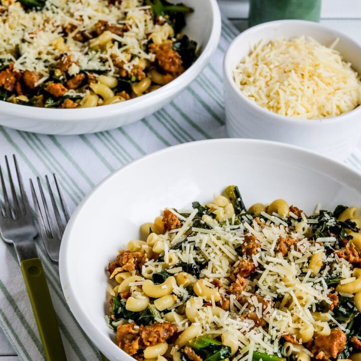 Italian Sausage Pasta with Collard Greens shown in two bowls with Parmesan on the side.