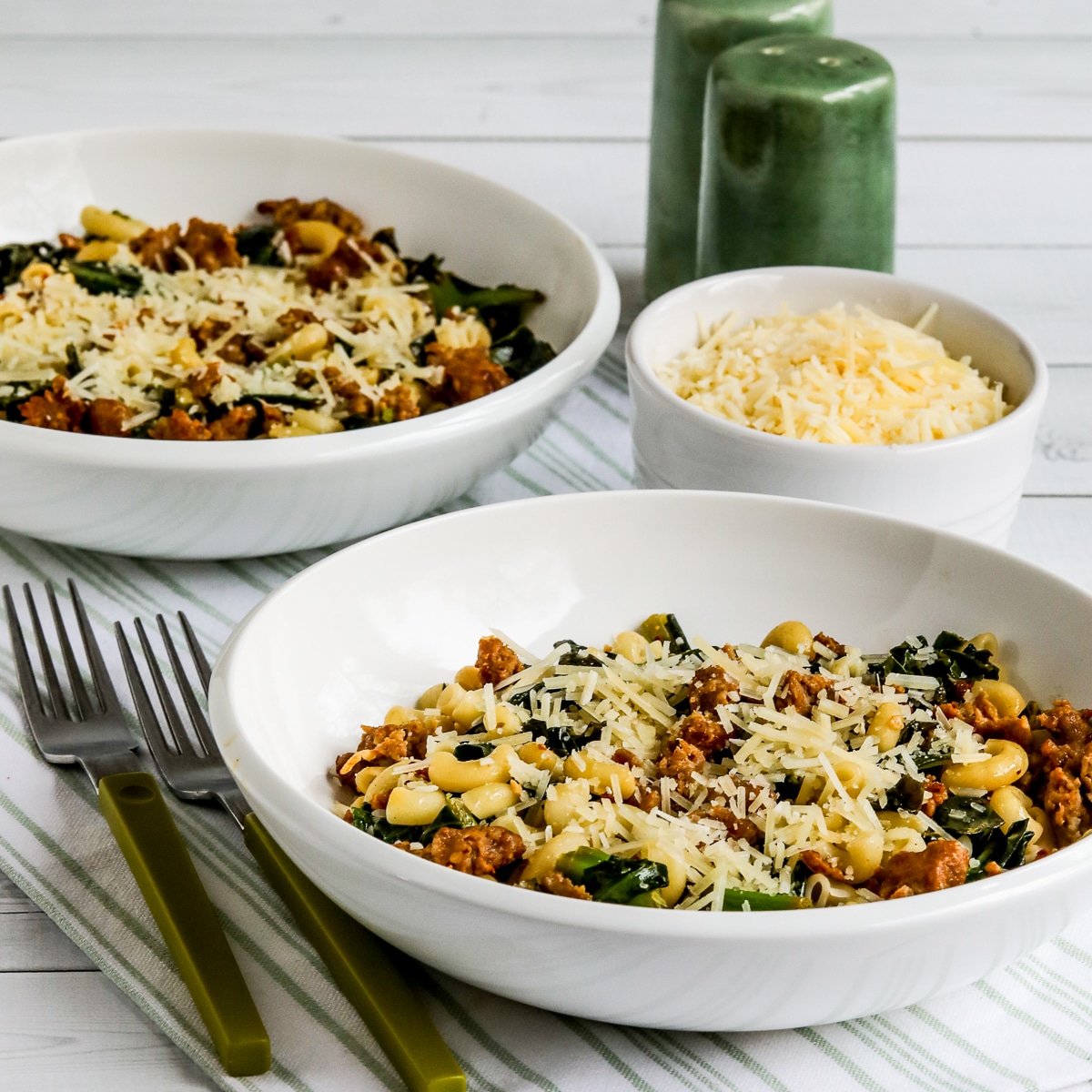 Italian Sausage Pasta with Collard Greens shown in two bowls with Parmesan cheese on the side.