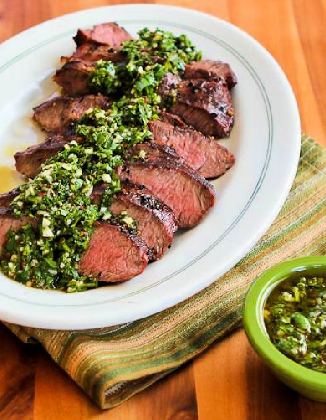 Grilled flat iron steak with chimichurri sauce presented on a platter with more chimichurri on the side.