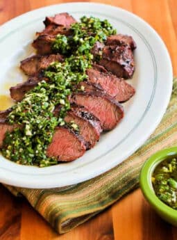 Square image of Grilled Flat Iron Steak with Chimichurri Sauce with sliced steak and sauce on serving plate.