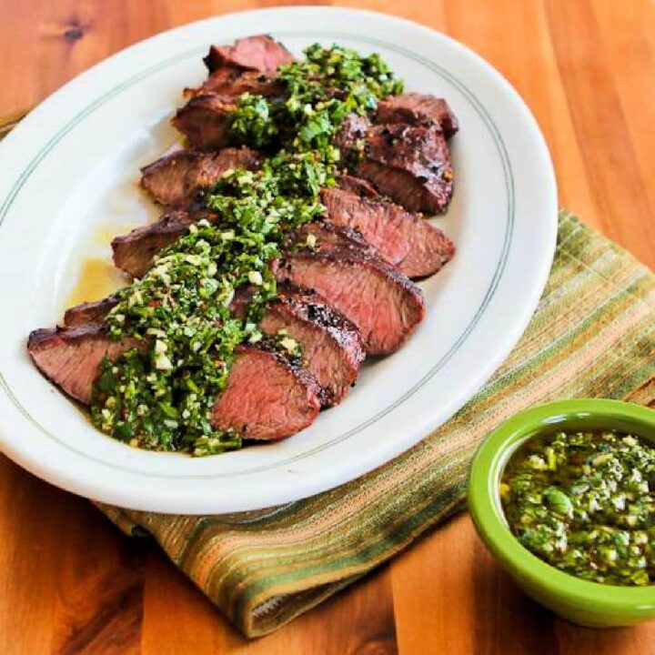 Square image of Grilled Flat Iron Steak with Chimichurri Sauce with sliced steak and sauce on serving plate.